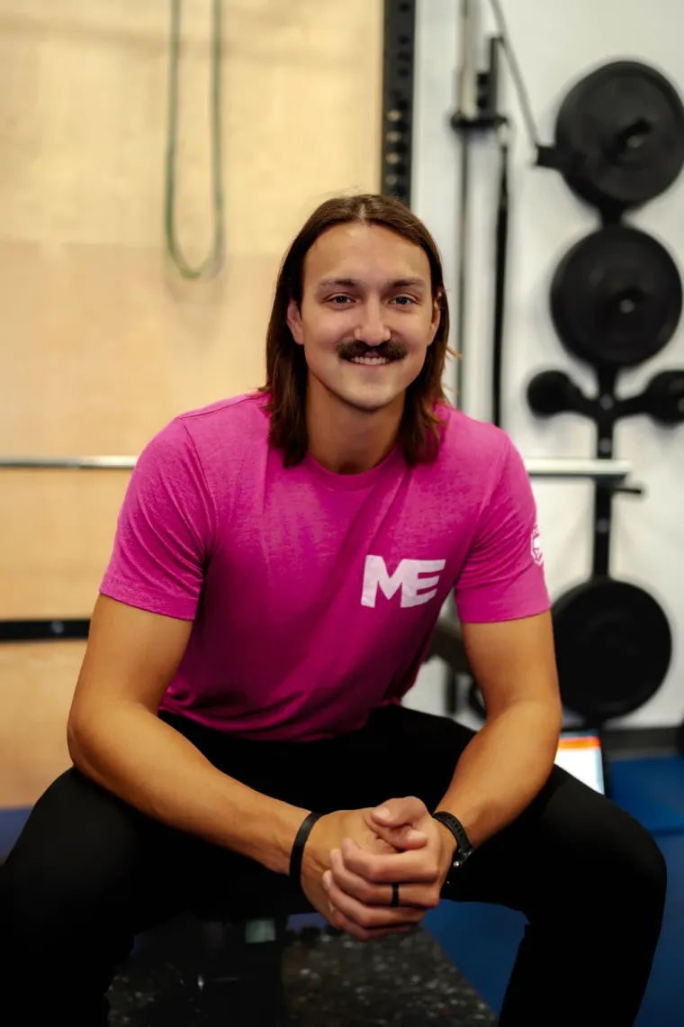 Alan, personal trainer at Studio ME Fitness, seated and smiling in the Northeast Minneapolis studio wearing a pink Studio ME shirt.