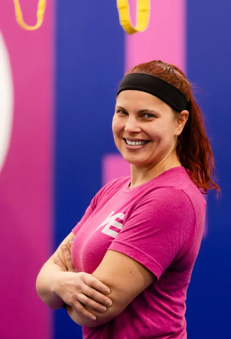 Chelsea, personal trainer at Studio ME Fitness, smiling in front of the pink and blue studio mural in Northeast Minneapolis.