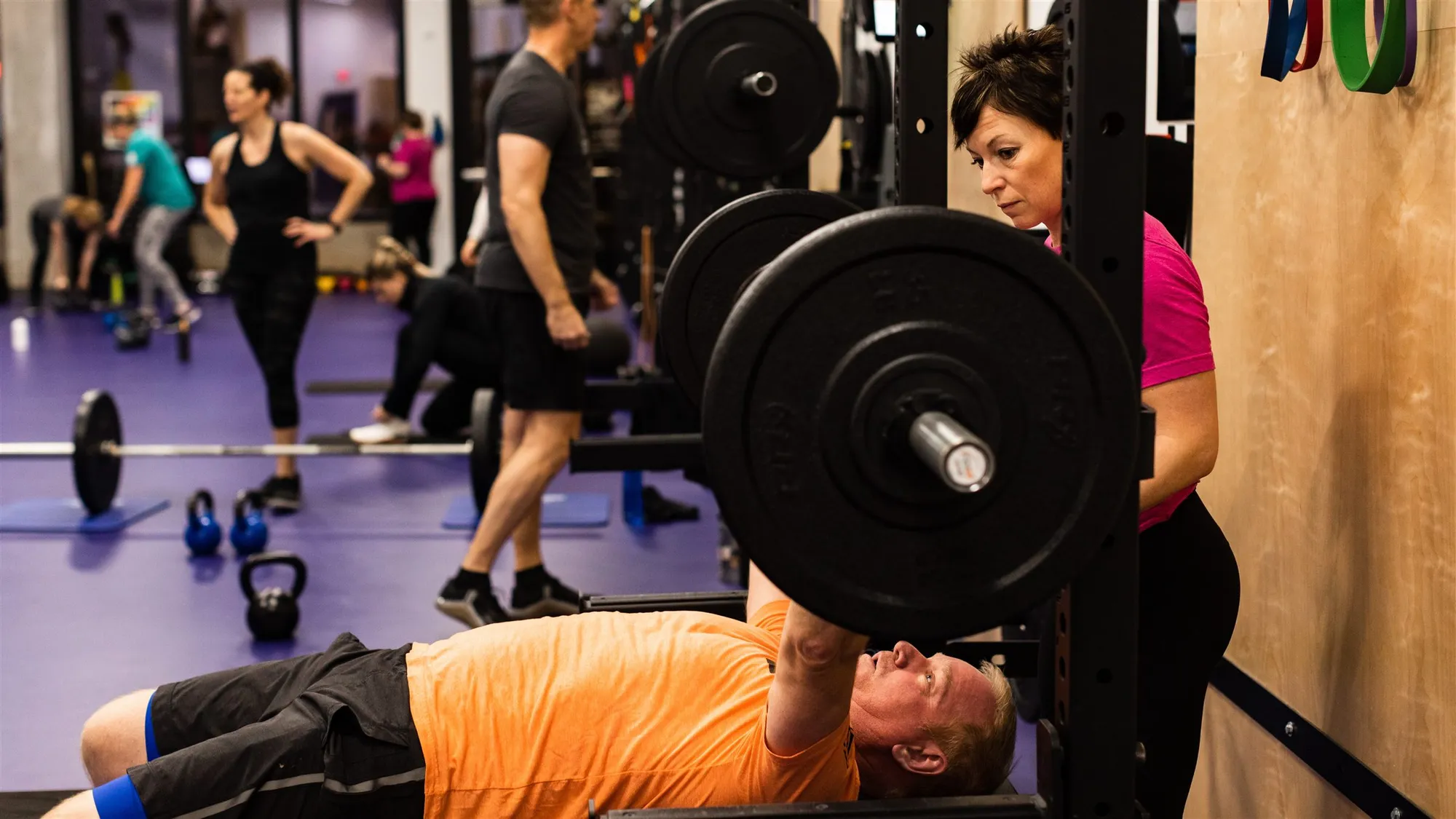 Megan Cooper spotting a client on the bench press during a private personal training session at Studio ME Fitness in Northeast Minneapolis, with other members training in the background.