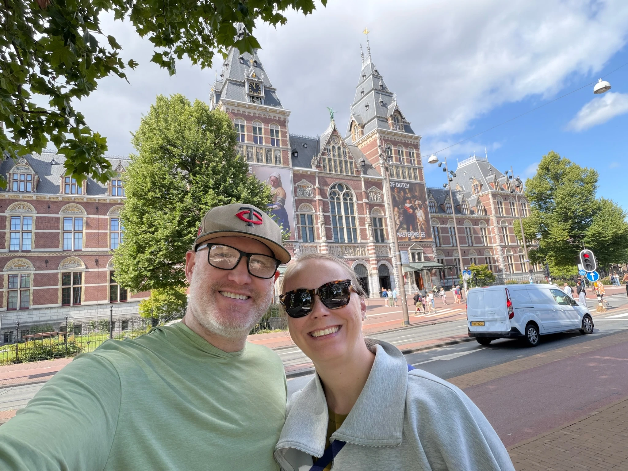 Ben and Elizabeth smiling in a selfie on a European city street, with a grand brick museum building with ornate spires in the background.