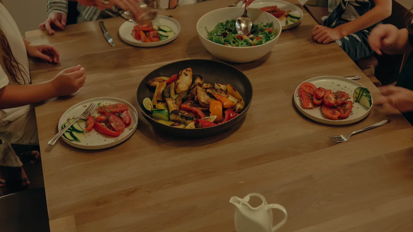 A family dinner table with roast vegetables and salad, hands serving