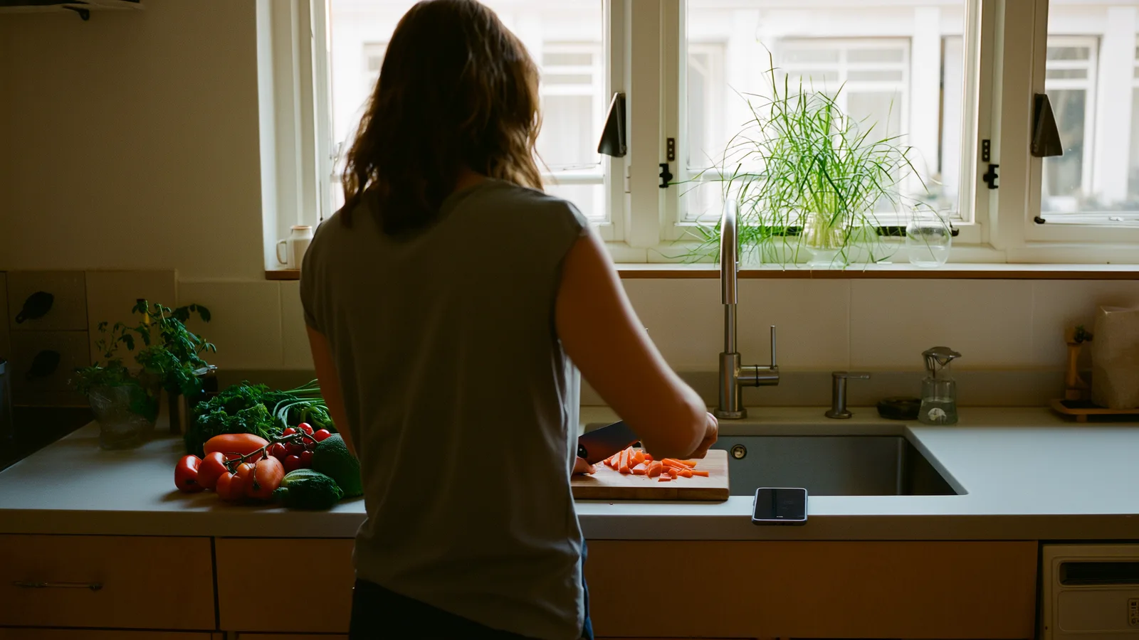 A morning kitchen counter with vegetables on a board, a notebook and a phone